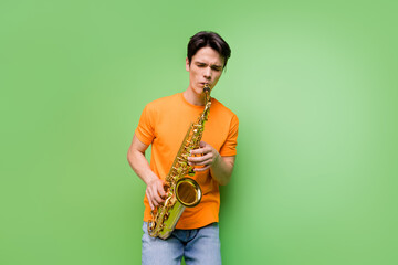 Photo of positive creative happy young man hold hands play saxophone isolated on green color background - obrazy, fototapety, plakaty