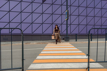 A beautiful girl with shopping bags is walking along a pedestrian crosswalk. Consumerism, shopping, shopping, lifestyle concept