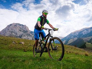 Obraz premium The cyclist rides in the mountains on a summer day. Bearded sportsman on a mountain bike. Outdoor activities