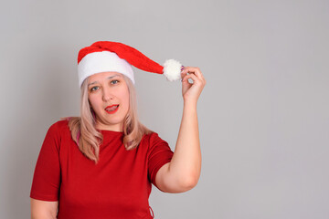 Adult sexy woman in a Santa hat with red lips and a seductive tongue on a gray background, copyspace