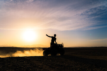 Silhouette shot of a man riding a quad bike or ATV in Hurghada, Egypt during sunset - obrazy, fototapety, plakaty