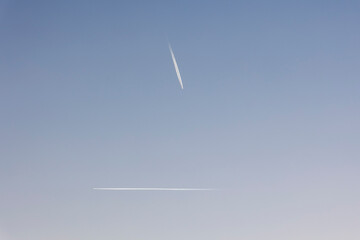 Contrails of two airplanes flying at right angles to each other in a blue sky in the morning