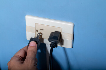 Man's hand plugging in a black wire. Latin, Colombian electrical outlet.