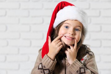 Little cute beautiful girl in red Santa hat smiling and looking into the camera.