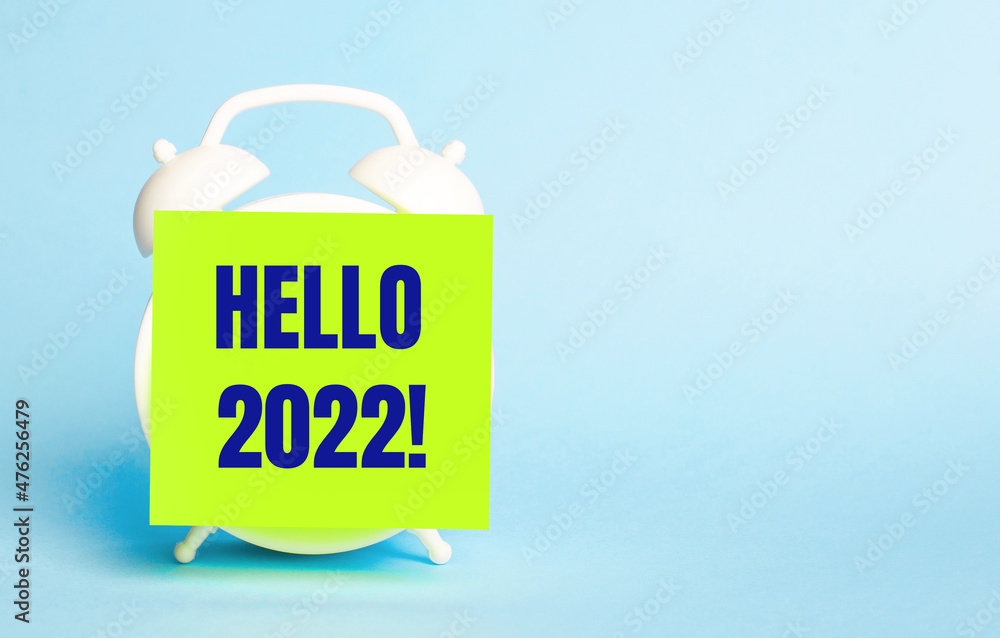 Poster on a blue background - a white alarm clock with a yellow sticker for notes with the text hello 2022