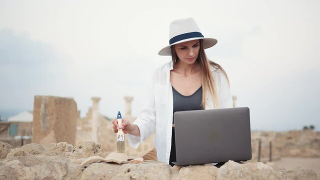Archeological Digging Site Discovery: Beautiful Female Archaeologist Doing Research, Using Laptop, Analysing Unearthed Ancient Civilization Culture Artifacts. Great Historian on Excavation Site.