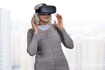 Surprised senior caucasian woman wearing virtual reality glasses on blurred background.