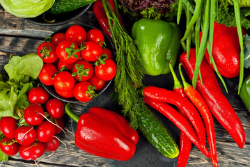 Cabbage, peppers, tomatoes, cucumbers, lettuce, cherry tomatoes, broccoli, arugula on a black background. variety of vegetables on a pile on a wooden table.