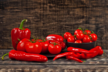 Red tomatoes and peppers on a black wooden background. Vegetables on an old shabby table. Copy space and place for text near vegetables.