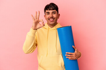 Young mixed race man holding a sport mat isolated on pink background cheerful and confident showing ok gesture.