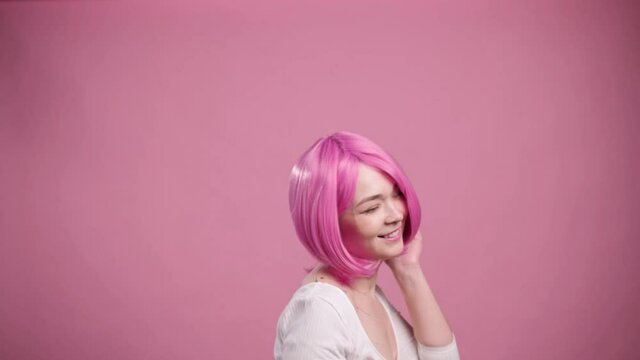 Smiling young pink haired woman dancing on pink background, slow motion.