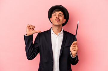 Young caucasian wizard man holding a wand isolated on pink background feels proud and self...