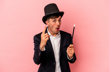 Young caucasian wizard man holding a wand isolated on pink background having an idea, inspiration...