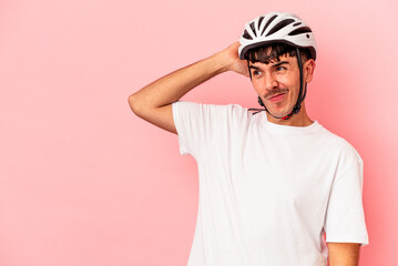 Young mixed race man wearing a helmet bike isolated on pink background touching back of head, thinking and making a choice.