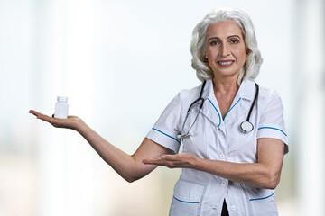 Senior doctor presenting pills standing on white background.