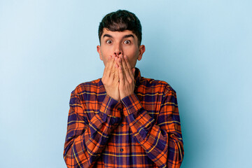 Young mixed race man isolated on blue background shocked, covering mouth with hands, anxious to discover something new.