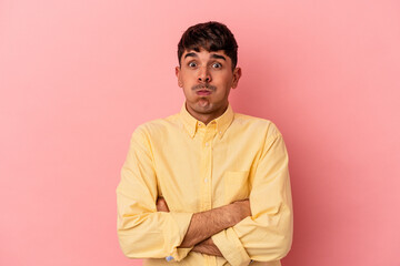Young mixed race man isolated on pink background blows cheeks, has tired expression. Facial expression concept.