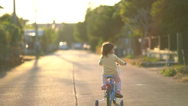 Backside of Asian toddler girl child learning to ride bicycle in sunny summer day, kid cycling at park, baby sport concept