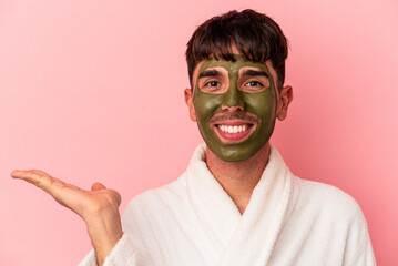 Young mixed race man wearing beauty facial mask isolated on pink background