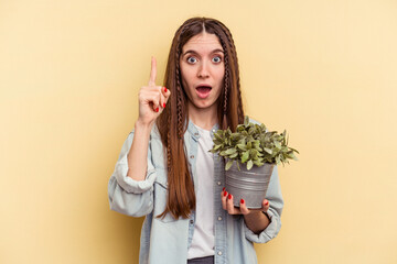 Young caucasian woman holding a plant isolated on yellow background having an idea, inspiration concept.