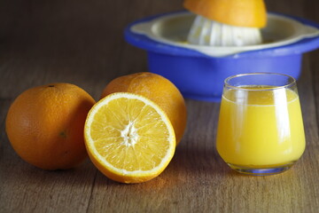 Blue squeezer and a glass of homemade orange juice and slice on wooden texture background. Close up.