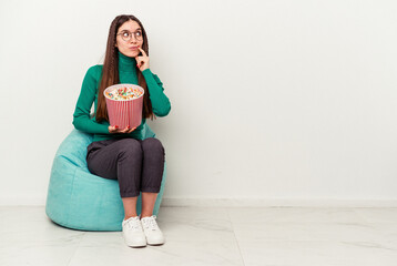 Young caucasian woman eating popcorns on a puff isolated on white background relaxed thinking about something looking at a copy space.