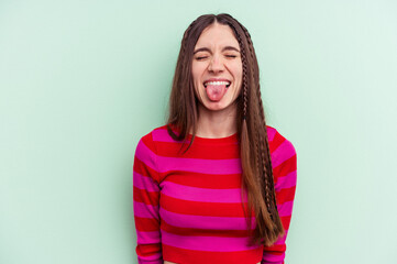 Young caucasian woman isolated on green background funny and friendly sticking out tongue.