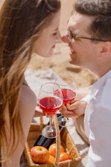 a couple of a man and a woman walk along the beach and have a picnic on the sand on the seashore or ocean. beautiful and young European man and woman on a romantic walk in nature drink wine and enjoy