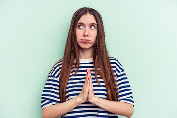 Young caucasian woman isolated on green background praying, showing devotion, religious person...