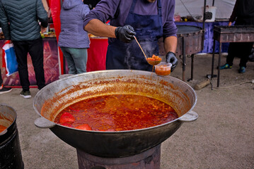 A ladle of Ukrainian borscht. Big cauldron with the Ukrainian national dish. The cook puts a portion of the traditional borscht into the container. Street food fair, event, festival. Ukraine.