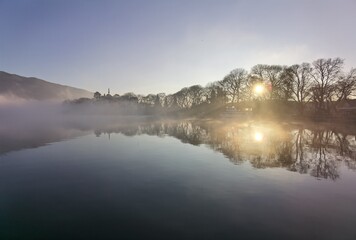 Fototapeta na wymiar fog in lake pamvotis of ioannina city greece in winter morning sunrise among leafless trees