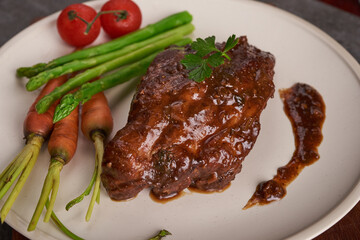 Pork roasted, grilled spare ribs from a summer BBQ served with Vegetables, asparagus, baby carrots, fresh tomatoes and  spices. smoked ribs in white plate on stone background . top view.