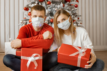 Couple man and woman with hygiene mask sit close to each other and look at camera for celebrating of Christmas during pandemic of Covid-19.