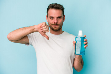 Young caucasian man holding mouthwash isolated on blue background showing a dislike gesture, thumbs down. Disagreement concept.