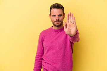 Young caucasian man isolated on yellow background standing with outstretched hand showing stop...