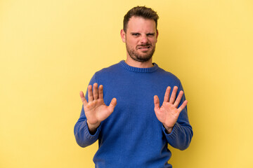 Young caucasian man isolated on yellow background rejecting someone showing a gesture of disgust.