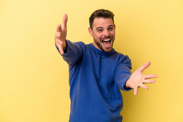 Young caucasian man isolated on yellow background feels confident giving a hug to the camera.