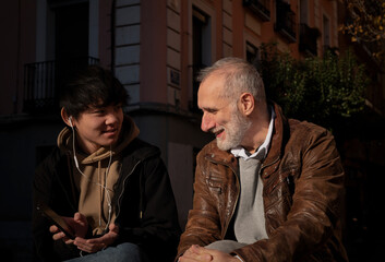 Asian teenage boy and Caucasian adult man chatting on street. Madrid. Spain