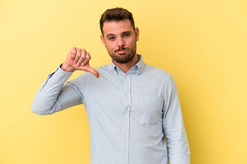 Young caucasian man isolated on yellow background showing a dislike gesture, thumbs down....