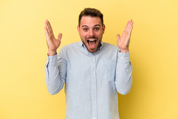 Fototapeta premium Young caucasian man isolated on yellow background receiving a pleasant surprise, excited and raising hands.