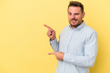 Young caucasian man isolated on yellow background shocked pointing with index fingers to a copy space.