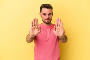Young caucasian man isolated on yellow background standing with outstretched hand showing stop...