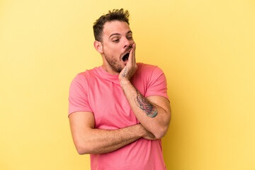 Young caucasian man isolated on yellow background yawning showing a tired gesture covering mouth with hand.