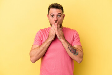 Young caucasian man isolated on yellow background shocked covering mouth with hands.