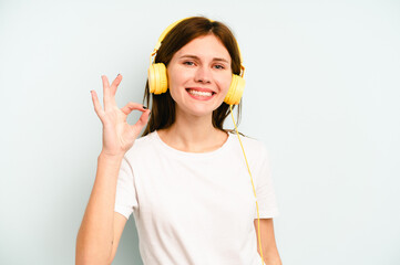 Young English woman listening to music isolated on blue background cheerful and confident showing...