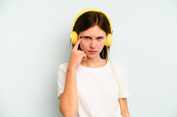 Young English woman listening to music isolated on blue background pointing temple with finger, thinking, focused on a task.