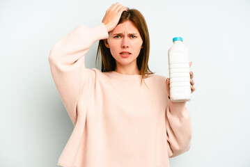 Young English woman holding a bottle of milk isolated on blue background being shocked, she has remembered important meeting.