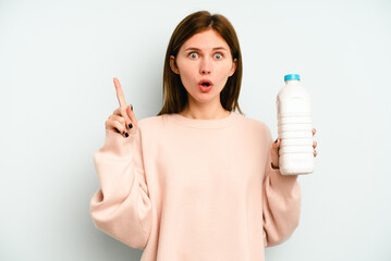 Young English woman holding a bottle of milk isolated on blue background having some great idea, concept of creativity.