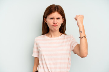 Young English woman isolated on blue background showing fist to camera, aggressive facial expression.