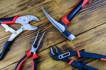 Hammer, adjustable water pump pliers, needle nose pliers and locking pliers on a wooden background....